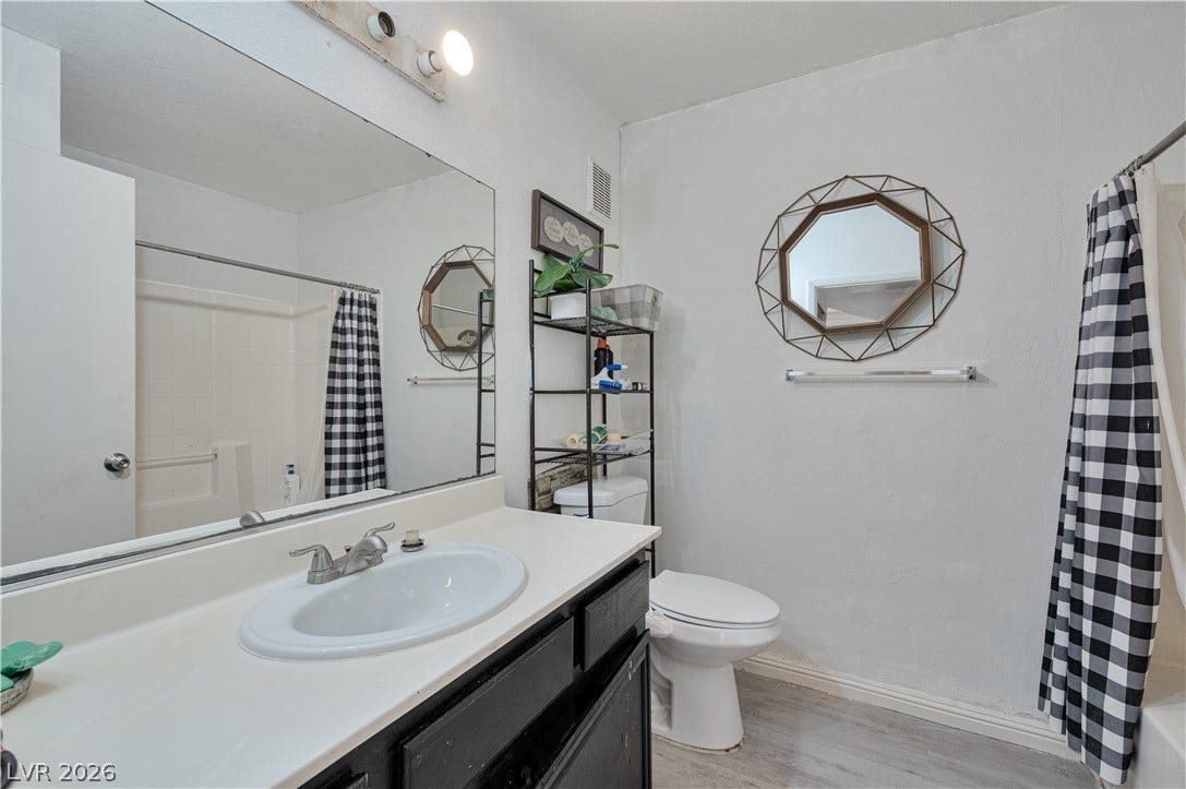 Functional bathroom layout features a large vanity mirror and wood-look laminate flooring.