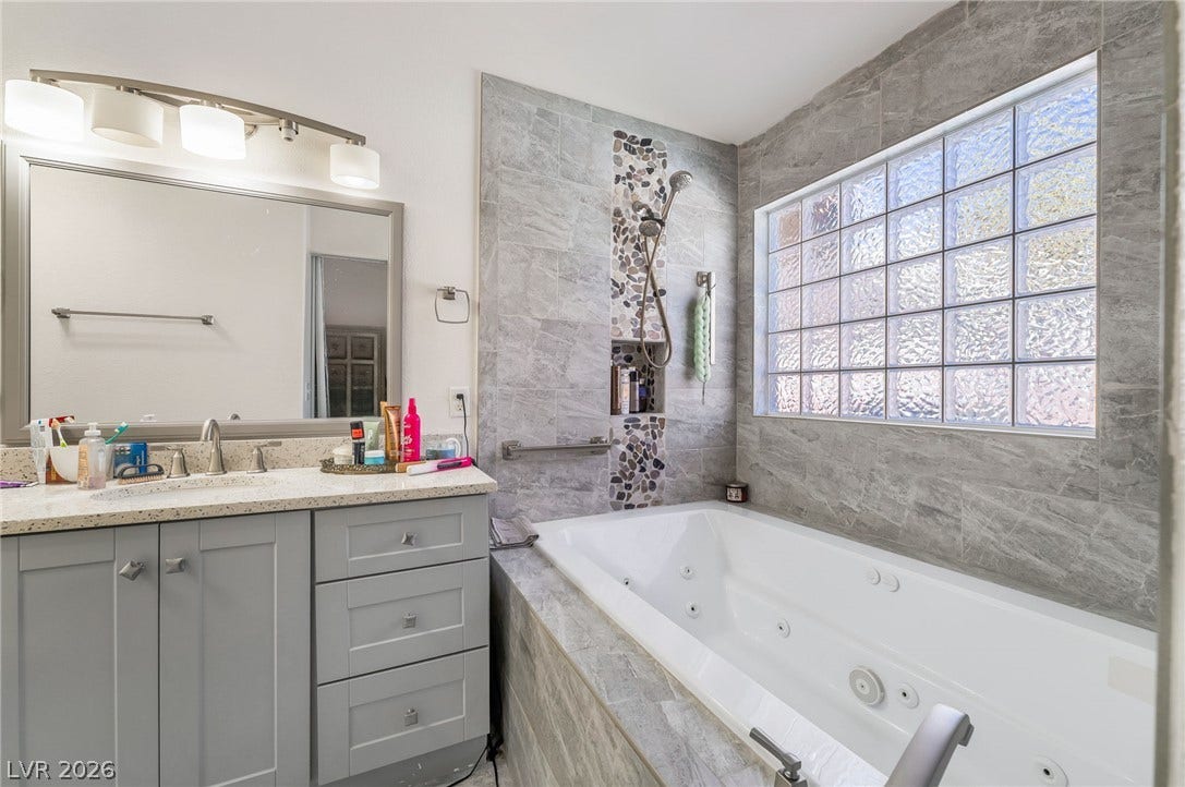 125 Heather Drive, Henderson, NV 89002 A deep soaking tub sits under a glass block window alongside a modern vanity.
