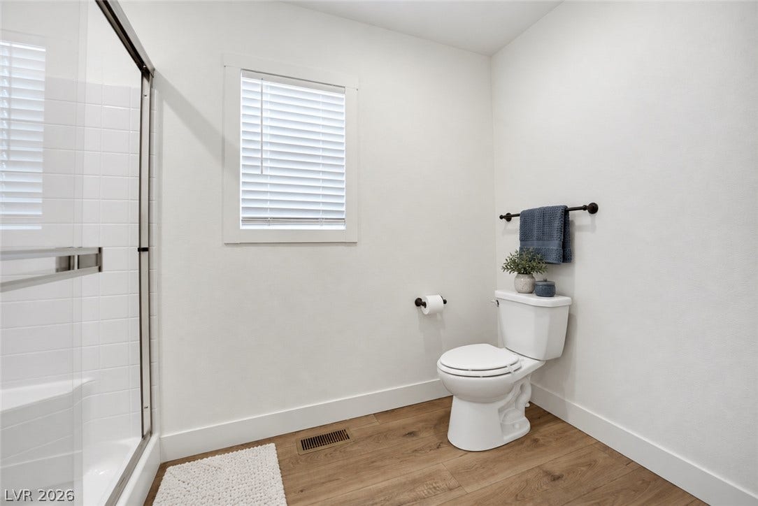 Crisp white walls and warm wood flooring define this streamlined bathroom design.