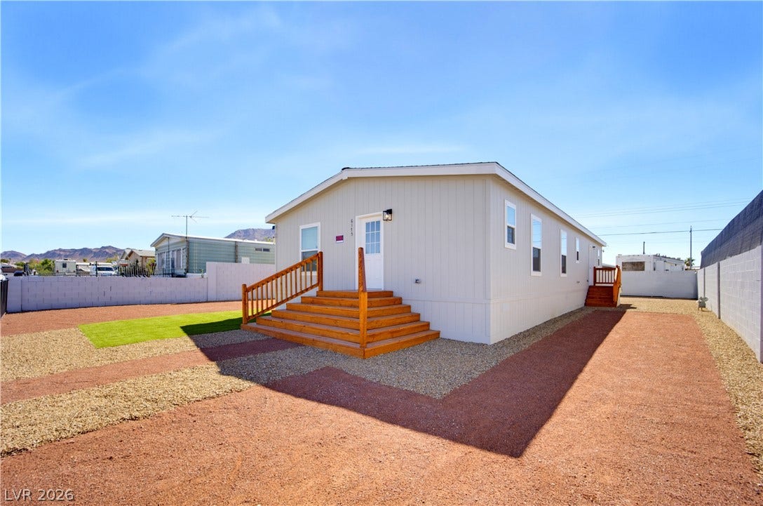 A manufactured home features low-maintenance desert landscaping and natural wood entry steps.