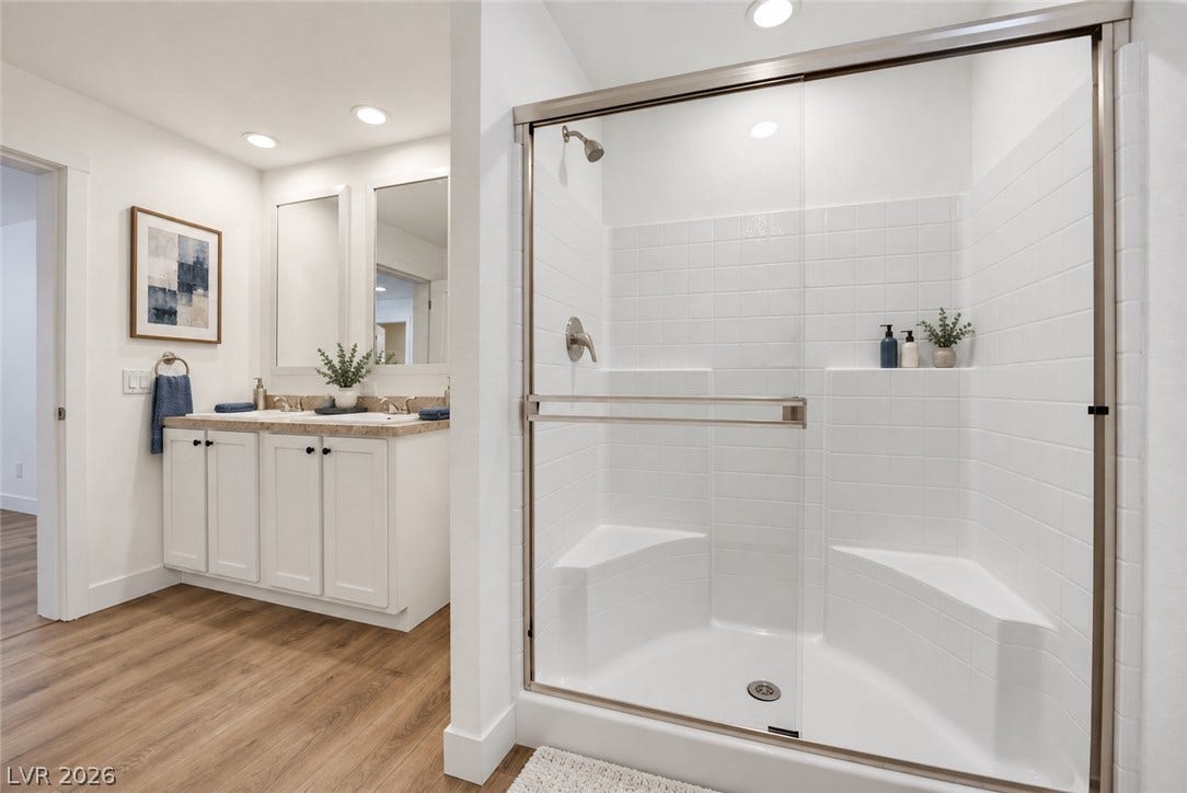 A contemporary bathroom features a glass-enclosed walk-in shower and a double vanity setup.