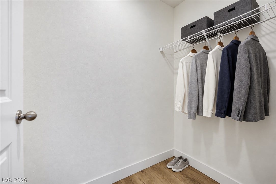 Ample hanging space and built-in shelving define this organized walk-in closet with warm wood floors.