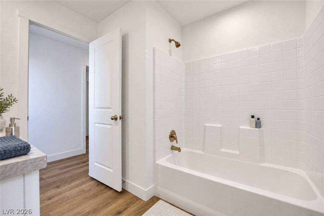 A classic tiled shower and tub combination integrates seamlessly with the warm wood-look flooring.