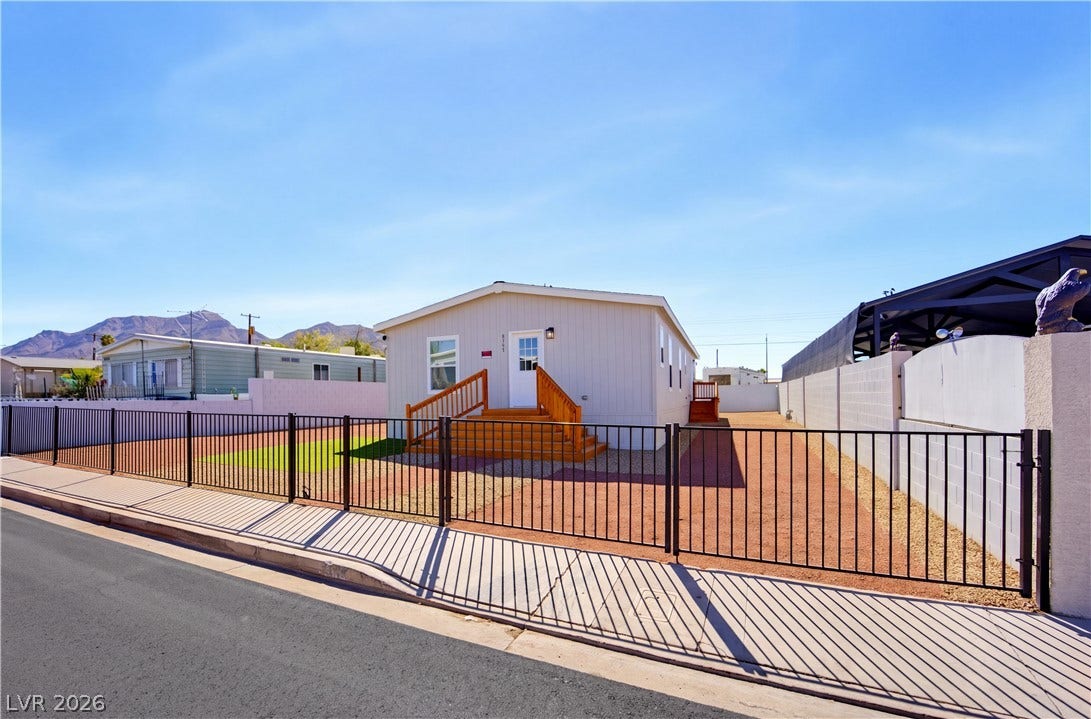 Gated metal fencing encloses a neat desert yard framed by distant mountain peaks.