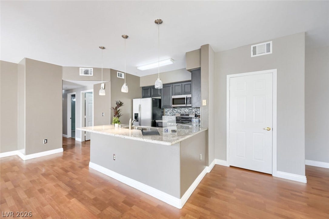 7173 S Durango Drive, #212, Las Vegas, NV 89113 Polished hardwood floors anchor an open kitchen layout bordered by sleek stone countertops.