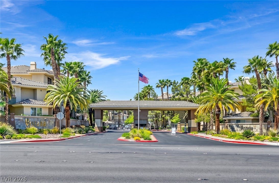 7173 S Durango Drive, #212, Las Vegas, NV 89113 Palm trees frame the gated stone entry structure under a clear blue sky.
