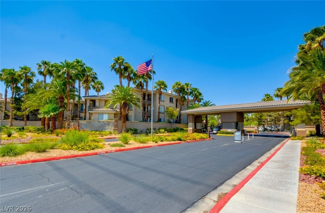 7173 S Durango Drive, #212, Las Vegas, NV 89113 Palm trees frame the paved entry drive leading toward a gated residential entrance.
