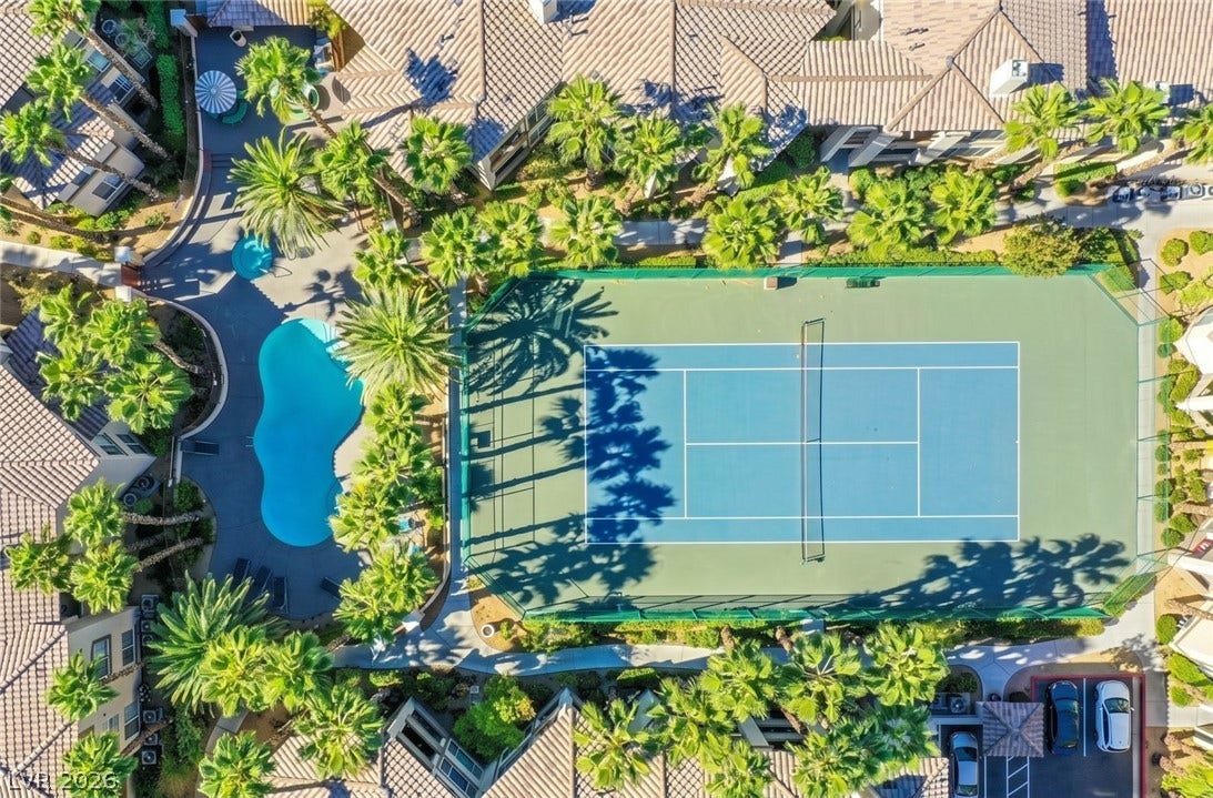 7173 S Durango Drive, #212, Las Vegas, NV 89113 An aerial perspective showcases a tennis court alongside a sparkling swimming pool surrounded by palm trees.