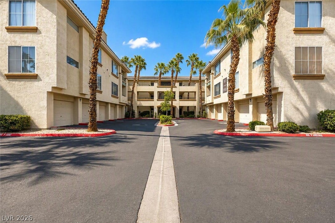 7173 S Durango Drive, #212, Las Vegas, NV 89113 Multi-level residential buildings feature integrated garages bordering a paved central driveway framed by palm trees.