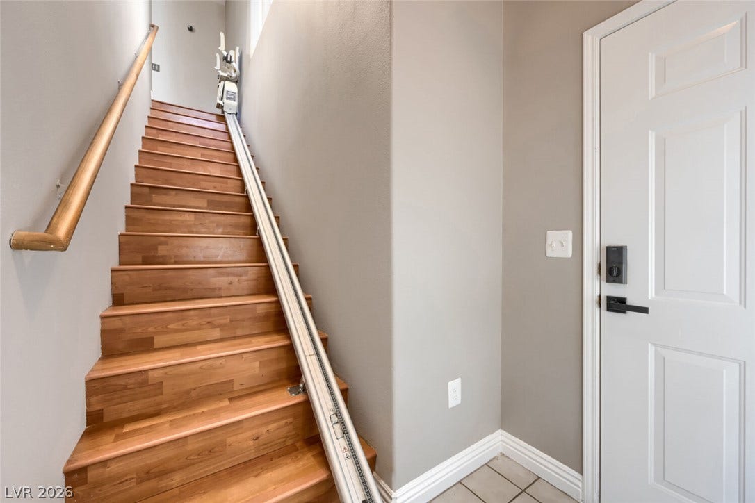 7173 S Durango Drive, #212, Las Vegas, NV 89113 A wooden staircase with a wooden handrail ascends next to a white interior door.
