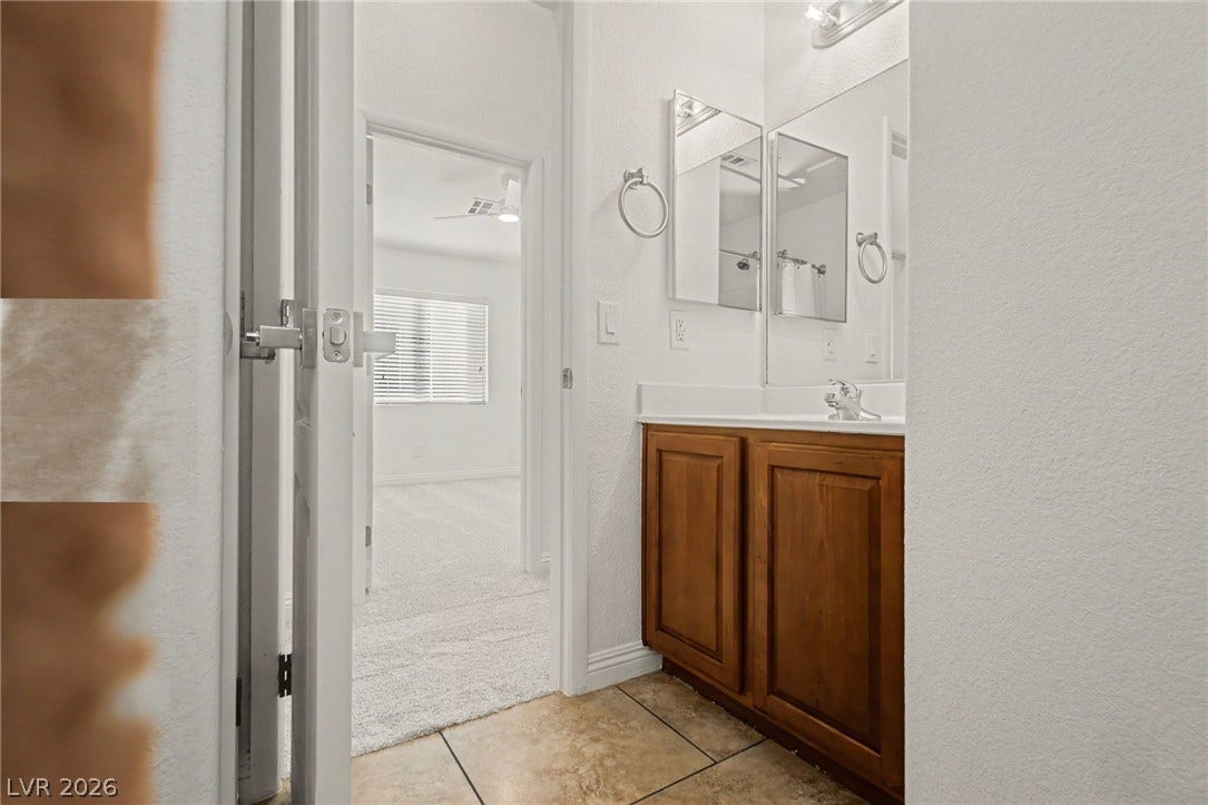 1555 Ward Frontier Lane, Henderson, NV 89002 An inviting vanity area features warm wood cabinetry and tile flooring next to a carpeted bedroom.