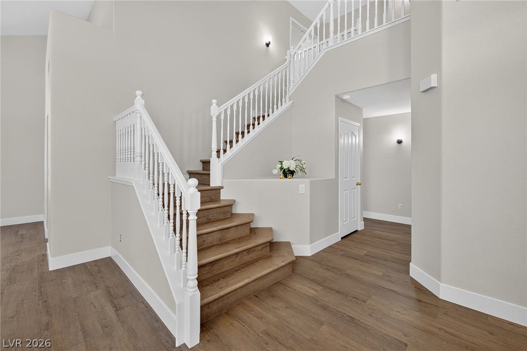 A grand, multi-level staircase with rich wood-look LVP treads and white banisters creates an inviting entryway.