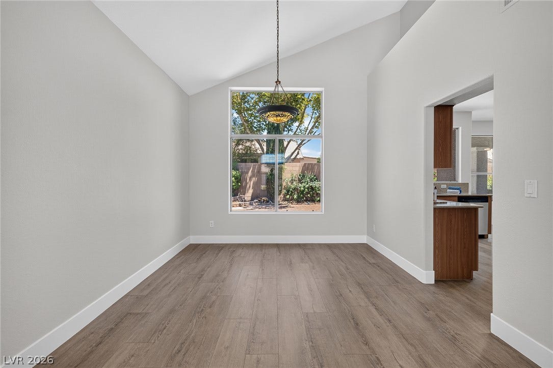Natural light pours into this dedicated dining space through an expansive window, highlighting vaulted ceilings and sleek wood-look Luxury Vinyl Plank flooring.