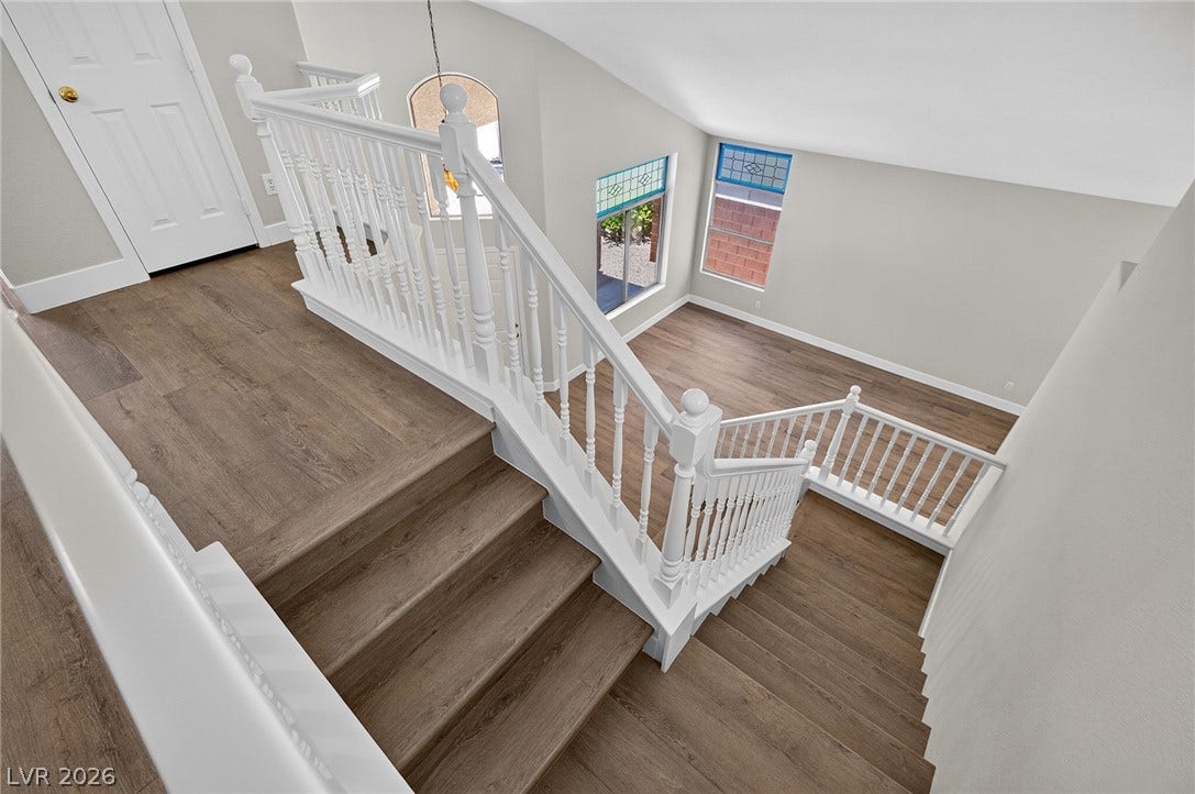Elegant white railings guide down to a spacious lower level with wood-plank style LVP flooring and sun-catching windows.