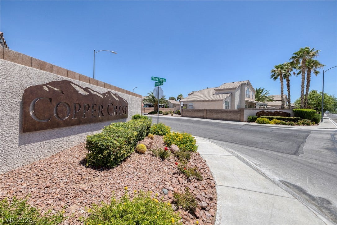 A well-maintained community entrance features desert landscaping and metal signage.