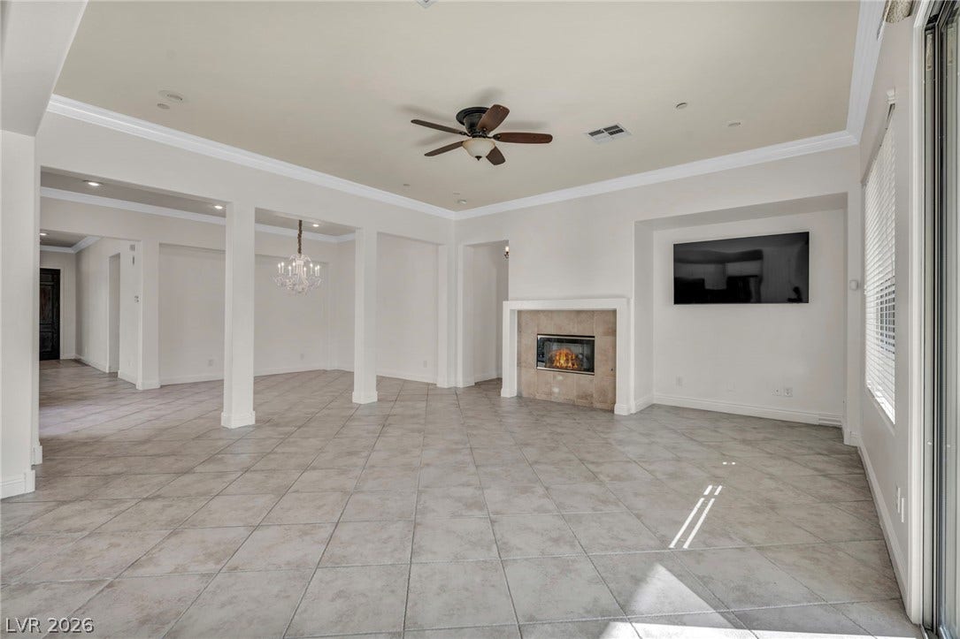 37 Stonemark Drive, Henderson, NV 89052 Unfurnished living room with baseboards, ornamental molding, a fireplace, visible vents, and ceiling fan with notable chandelier