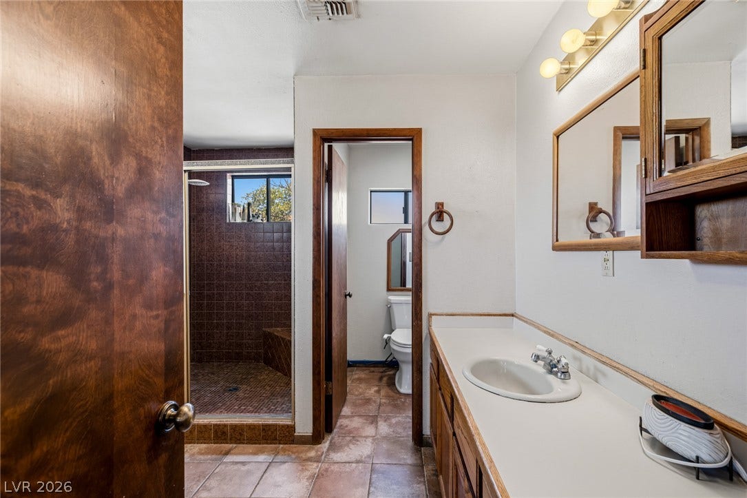 29 Cottonwood Drive, Blue Diamond, NV 89004 Functional bathroom layout features rich tile flooring and an integrated wooden vanity.