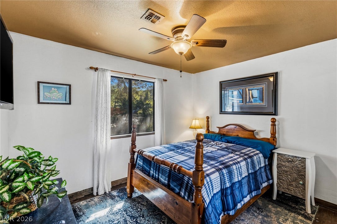 29 Cottonwood Drive, Blue Diamond, NV 89004 Natural light streams through a large window into this cozy bedroom with wood flooring.