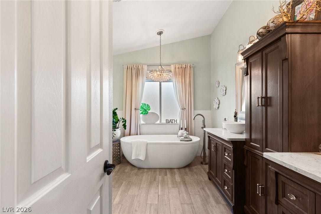 3950 Candleglow Court, Las Vegas, NV 89147 Vaulted ceilings and wood-look tile flooring frame this bathroom featuring a freestanding soaking tub.