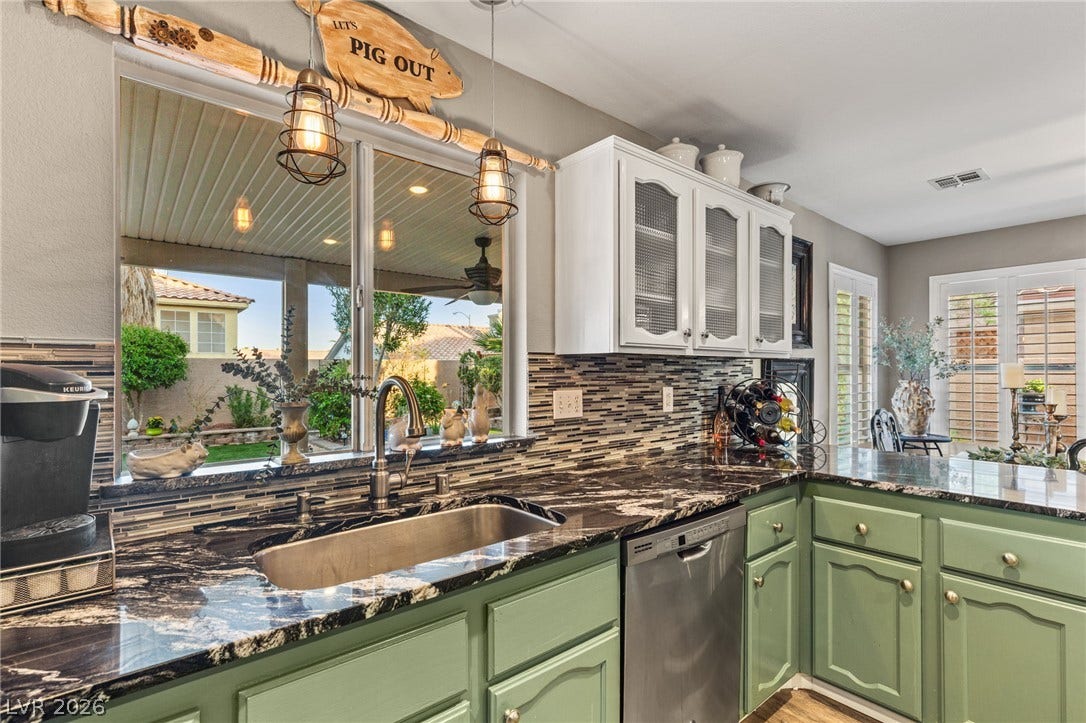 3950 Candleglow Court, Las Vegas, NV 89147 Striking dark stone countertops and a pass-through window define this functional kitchen space.