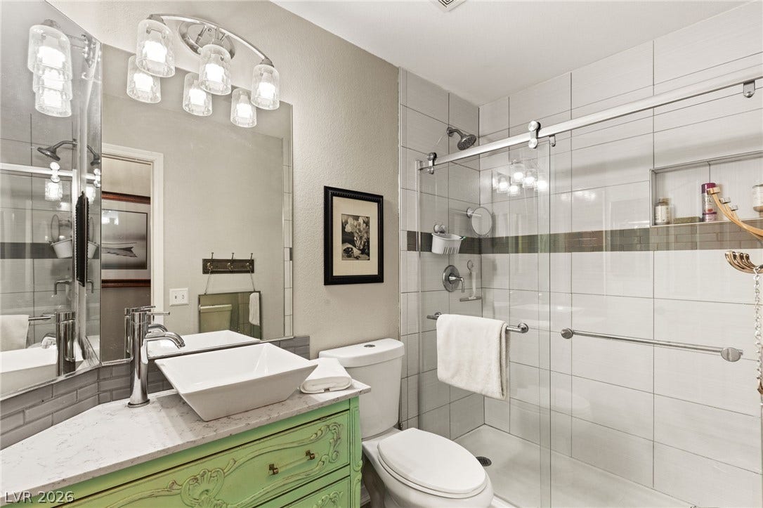 3950 Candleglow Court, Las Vegas, NV 89147 Modern tiled shower featuring sliding glass doors sits adjacent to a sleek stone-topped vanity.