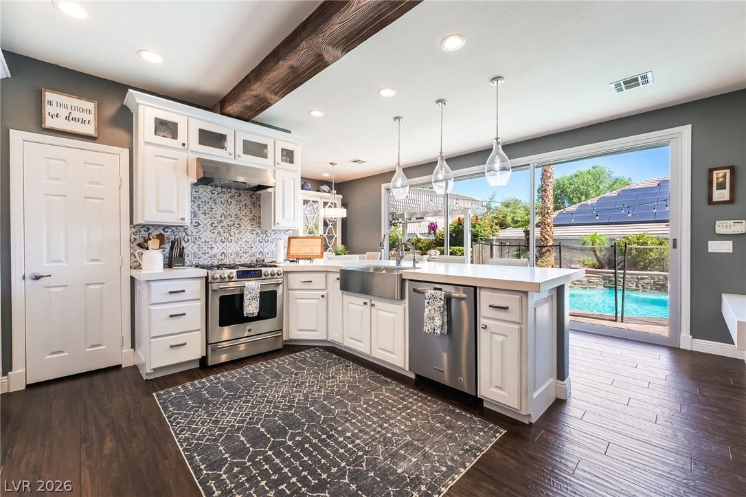 1892 Woodhaven Drive, Henderson, NV 89074 A well-lit kitchen with dark wood flooring features a farmhouse sink and gleaming stainless steel appliances, opening to a private backyard oasis with a swimming pool.