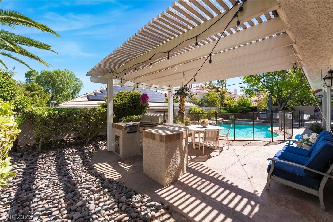 1892 Woodhaven Drive, Henderson, NV 89074 An inviting outdoor living space features a built-in barbecue station and a fenced swimming pool, all beneath a charming pergola.