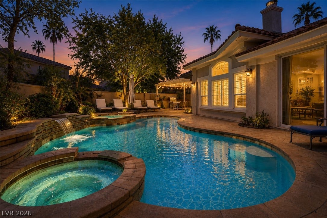 1892 Woodhaven Drive, Henderson, NV 89074 An illuminated backyard oasis boasts a freeform pool with a cascading waterfall and an inviting spa. Photo has safety pool fence removed.