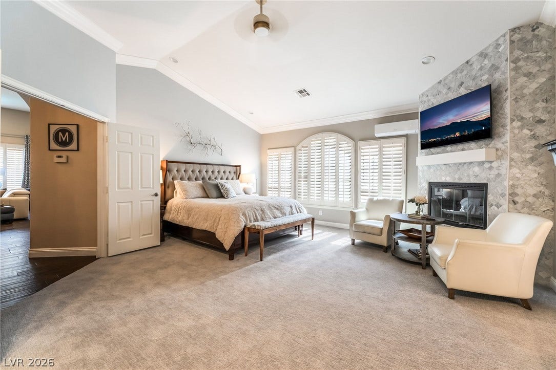 1892 Woodhaven Drive, Henderson, NV 89074 Experience luxurious comfort in this primary bedroom featuring a fireplace and plush carpet flooring.