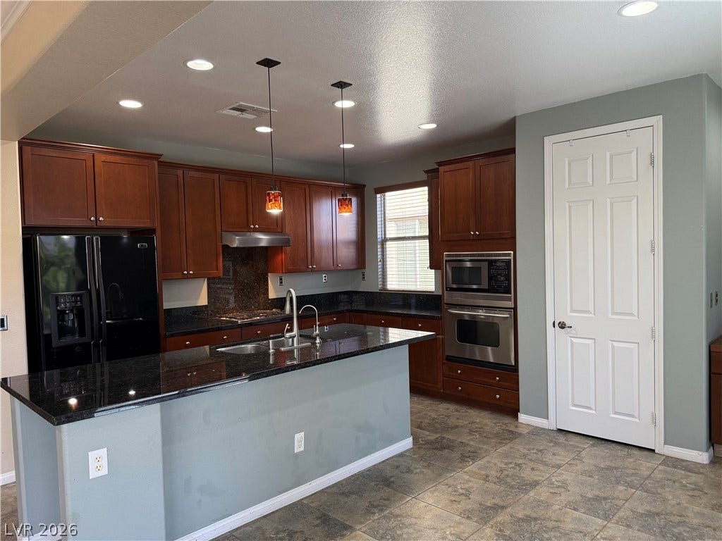 4327 Oasis Hill Avenue, North Las Vegas, NV 89085 Rich wood cabinetry and a central island highlight this functional cooking space with stone countertops.