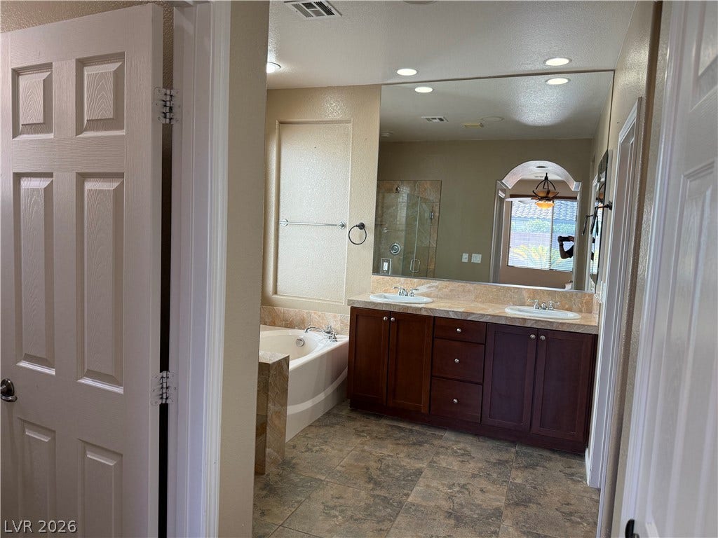 4327 Oasis Hill Avenue, North Las Vegas, NV 89085 Tile flooring leads past a soaking tub to a double vanity beneath recessed lighting.