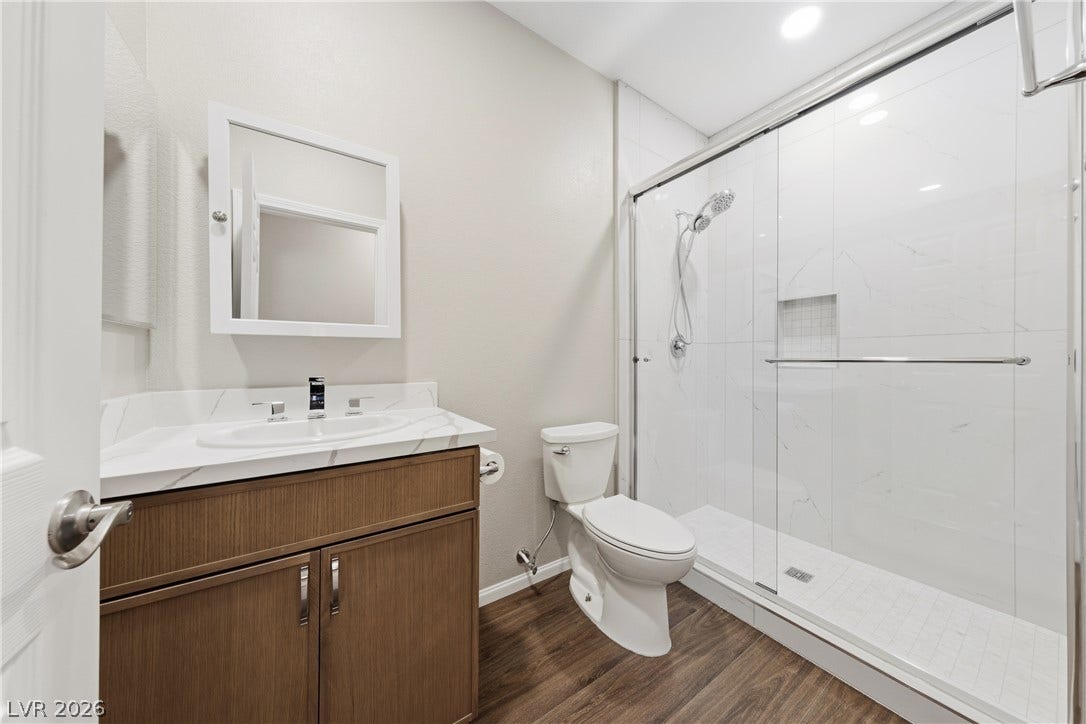 9613 Cherry Canyon Avenue, Las Vegas, NV 89129 A modern walk-in shower with sliding glass doors complements wood-look flooring and stone vanity counters.