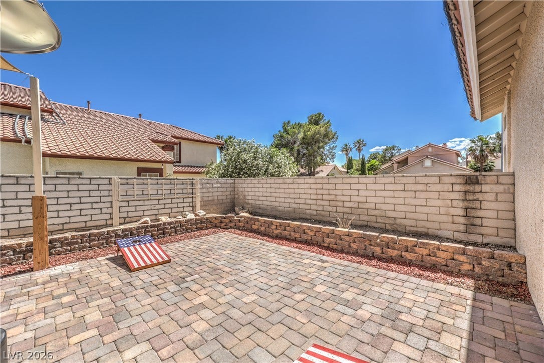 A spacious brick paver patio is enclosed by a privacy block wall under clear blue skies.