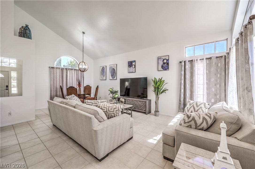 An open living room features vaulted ceilings, arched windows, and tile flooring throughout.