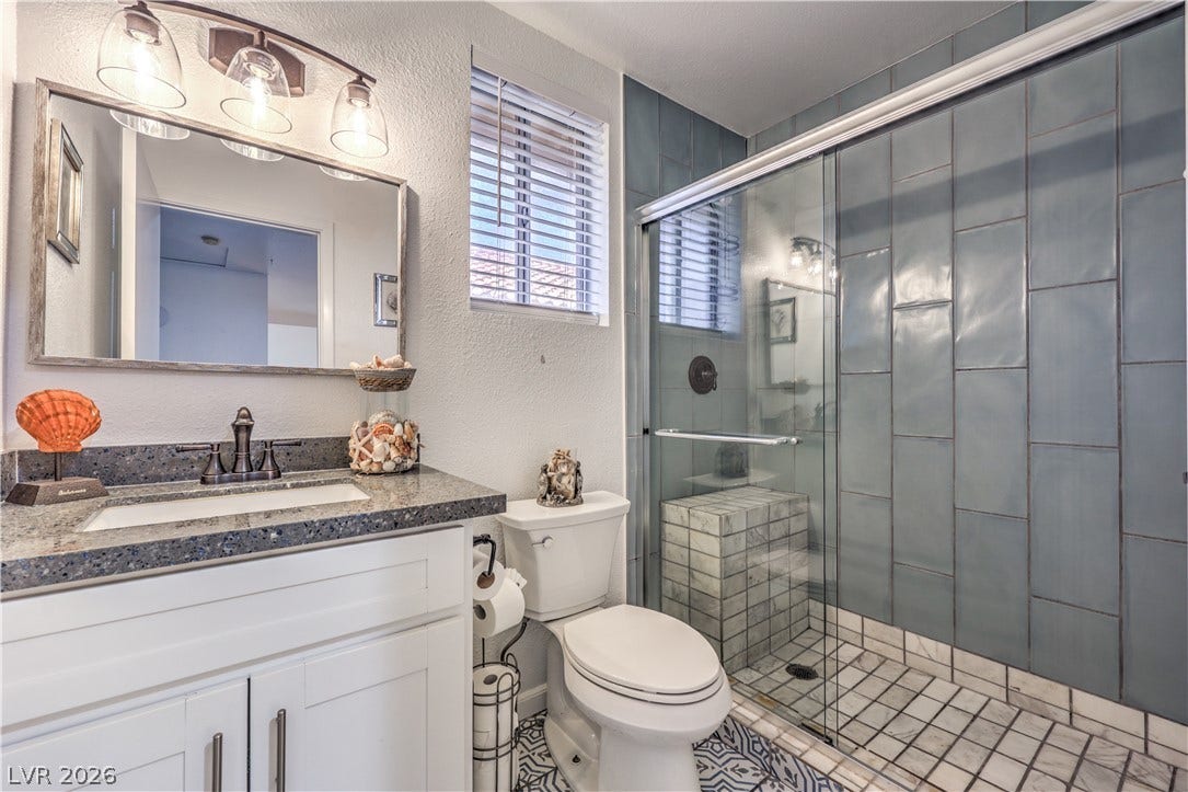 A modern tiled shower enclosure stands next to a vanity with stone counters.