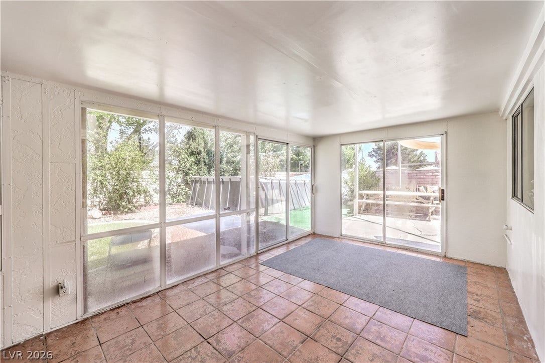 Sunlight streams through expansive glass doors onto rustic tile floors in this versatile sunroom.