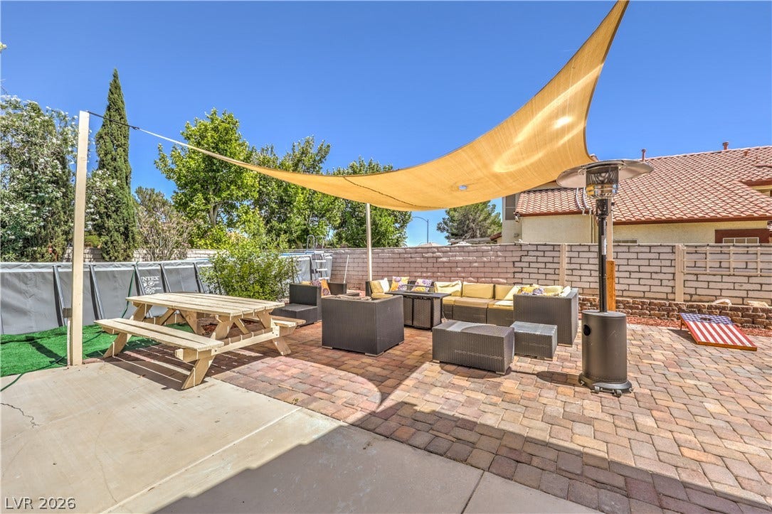 An inviting backyard patio paved with stone offers a serene setting under a sun sail.