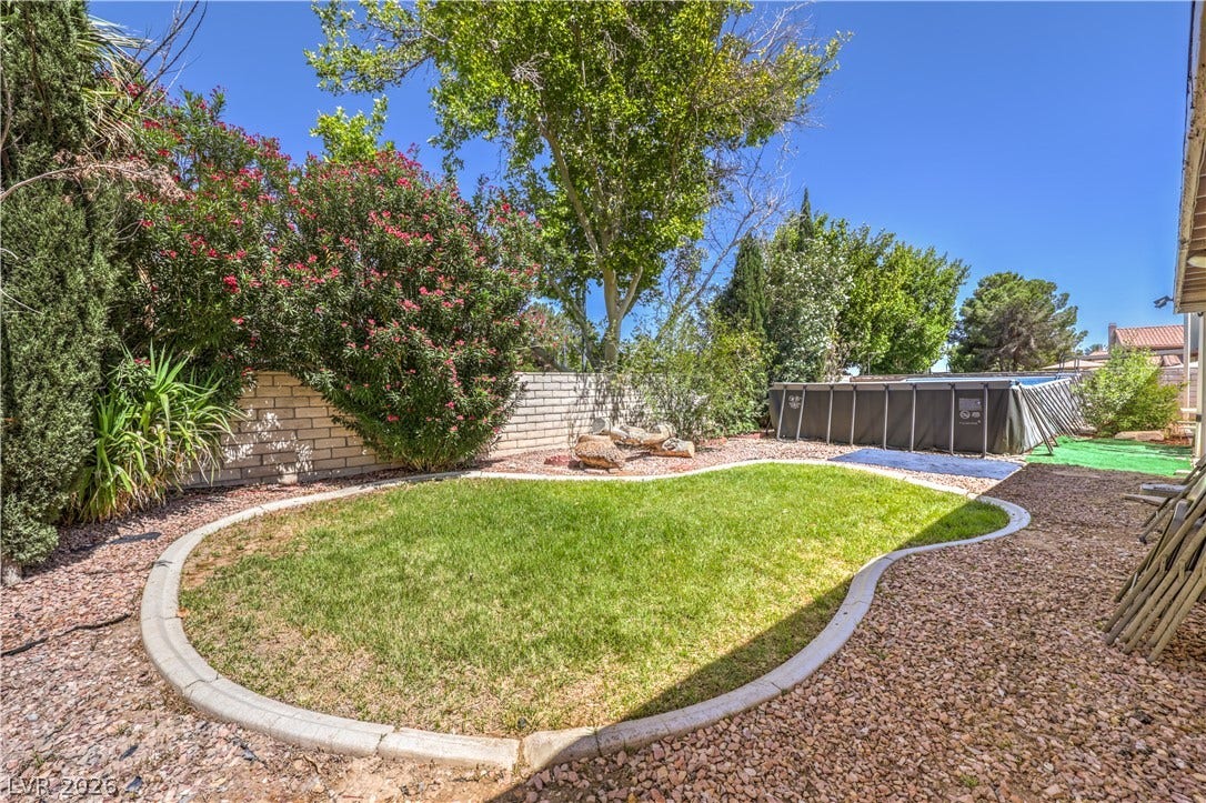 Mature trees and block wall fencing frame a private backyard with a curved lawn.