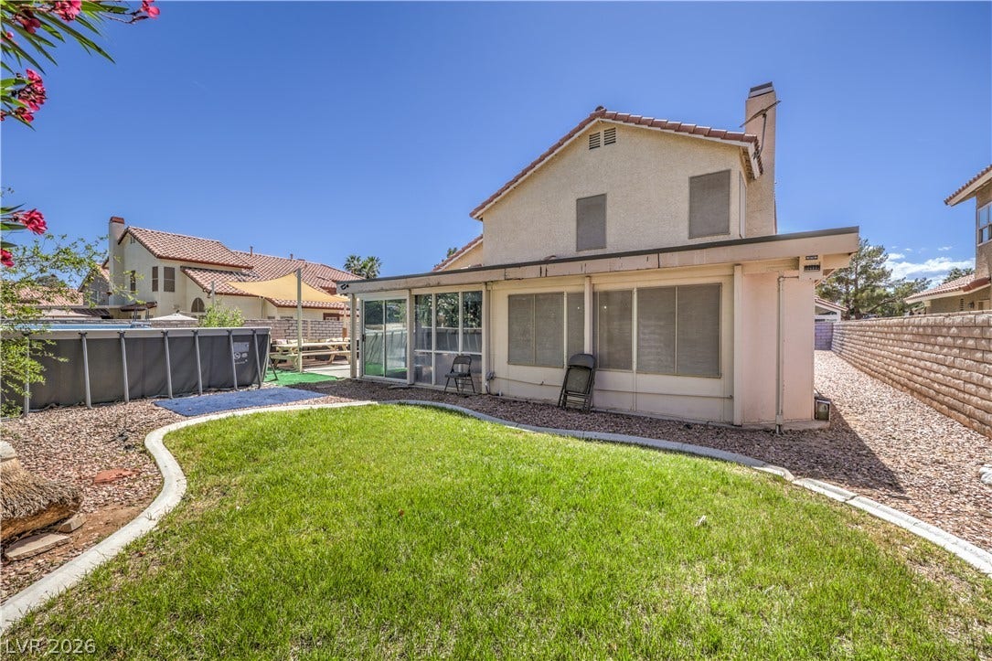 An enclosed patio overlooks the manicured green lawn and fenced rear yard.
