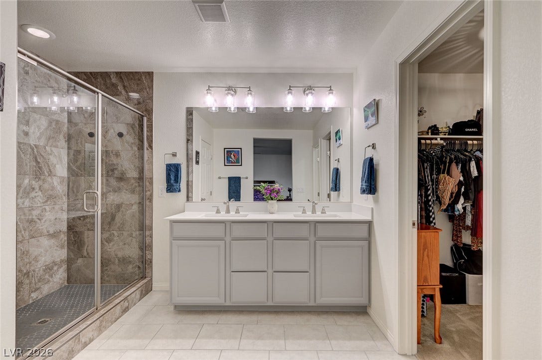 4114 Billowing Breeze Avenue, North Las Vegas, NV 89081 A spacious double vanity and a glass-enclosed walk-in shower define this tiled bathroom.