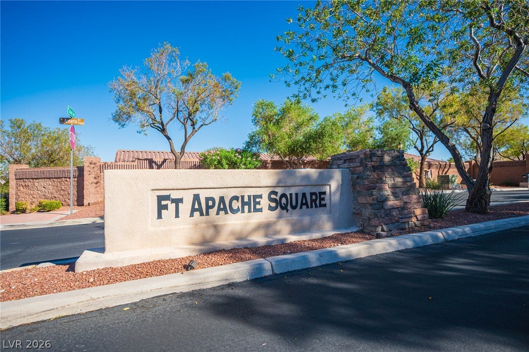 Mature trees frame the stone-accented neighborhood monument under a clear blue sky.