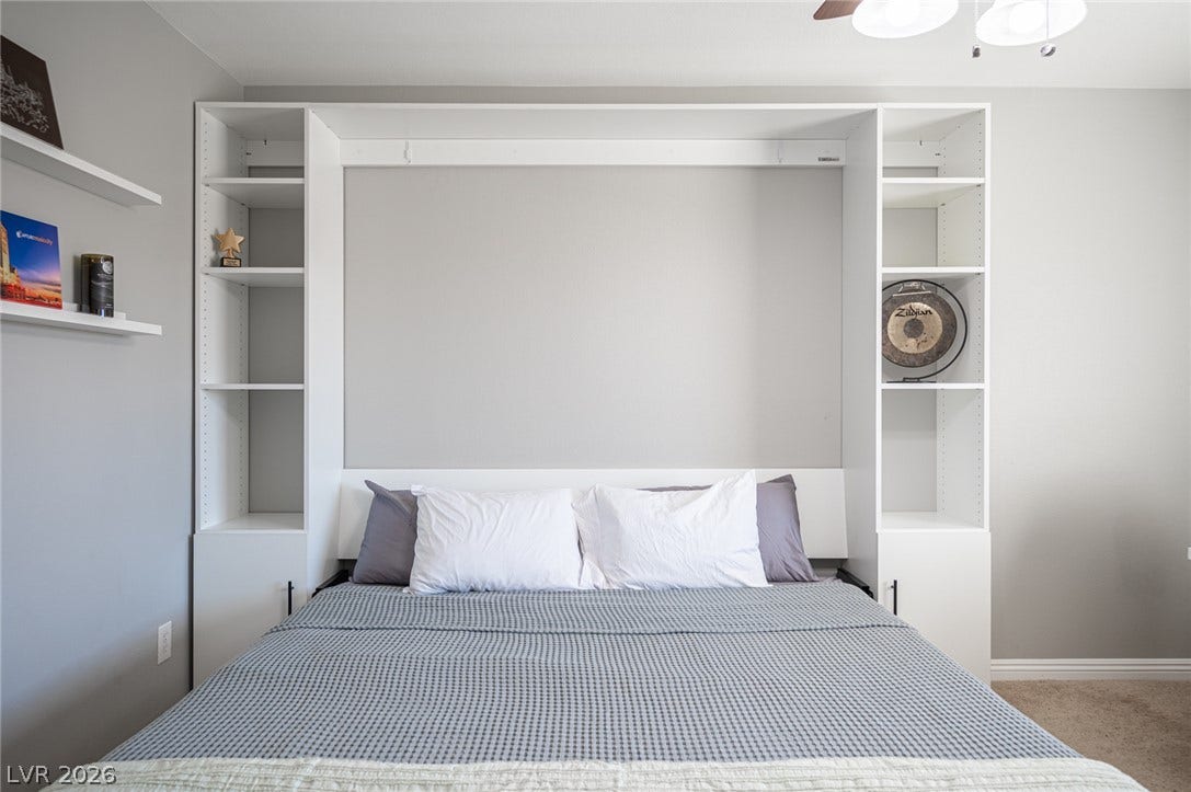 Custom built-in shelving surrounds a space-saving wall bed unit over soft carpet flooring.