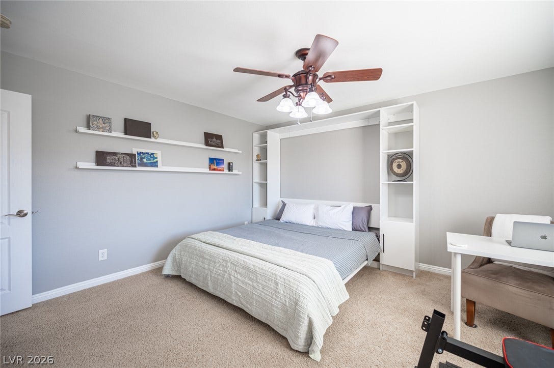 A versatile bedroom features neutral walls, built-in shelving, and plush carpeting.