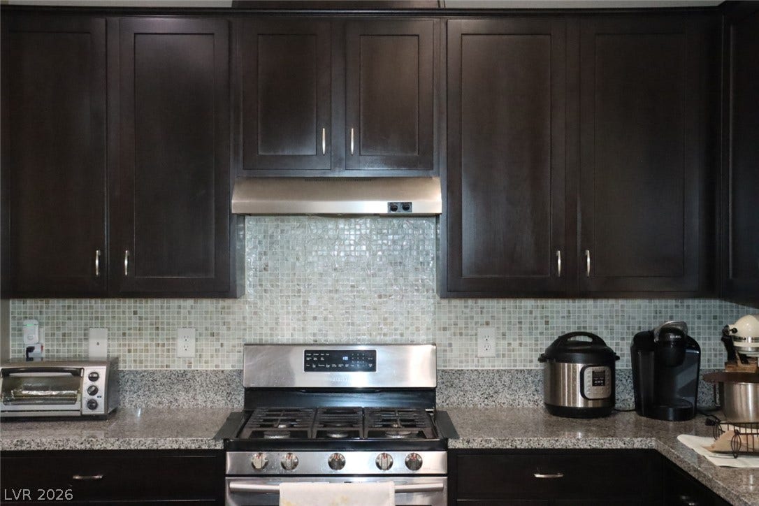 Rich dark cabinetry frames a mosaic tile backsplash and polished granite countertops.