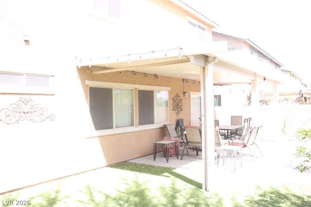 A covered concrete patio provides shade alongside the manicured grassy yard.
