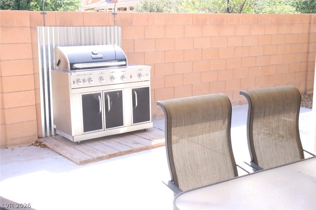 A spacious concrete patio is enclosed by a privacy wall featuring a built-in grilling area.