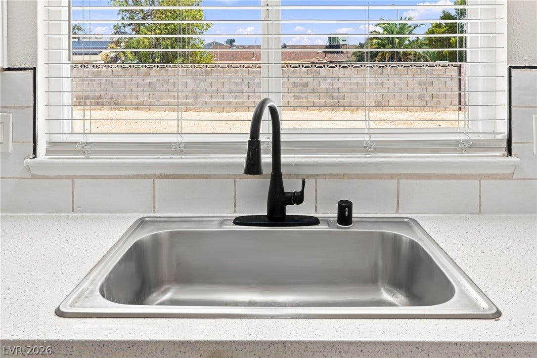A classic stainless steel basin sits below a window overlooking the backyard.