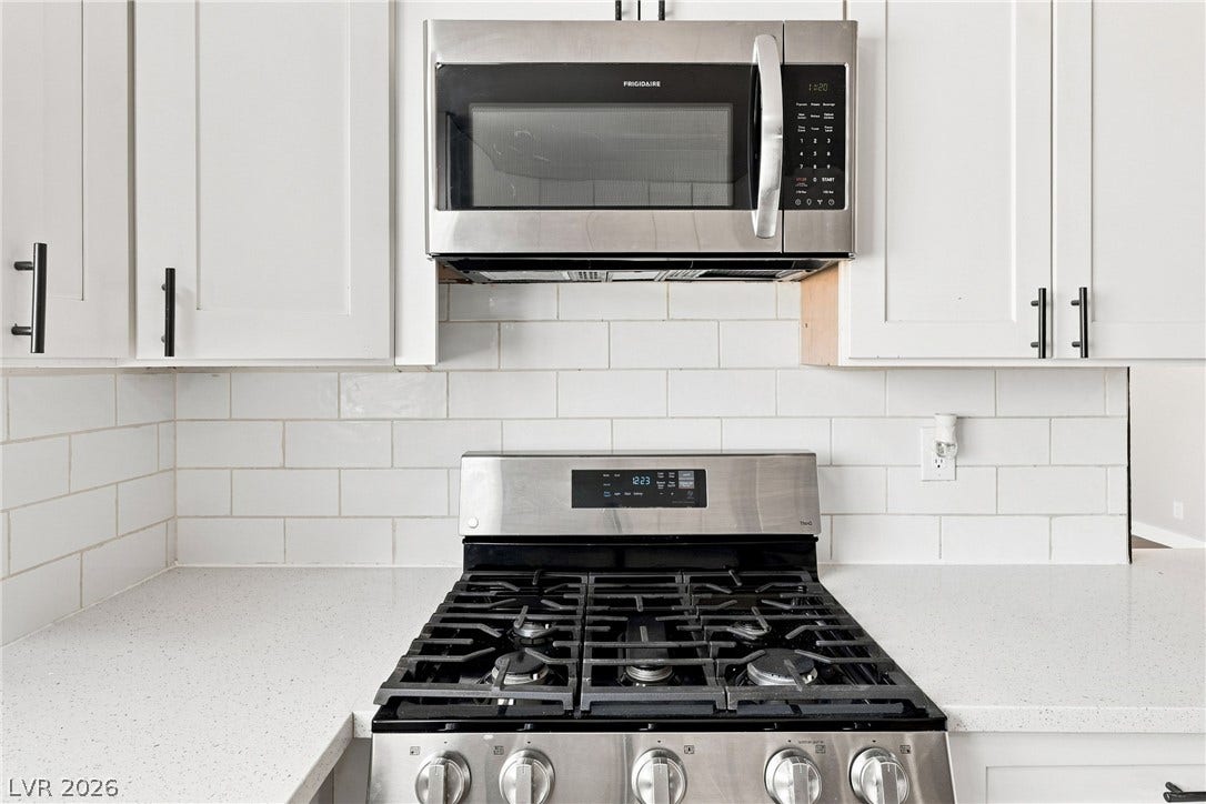 Modern cabinetry and stone countertops frame a high-quality gas range and built-in microwave.