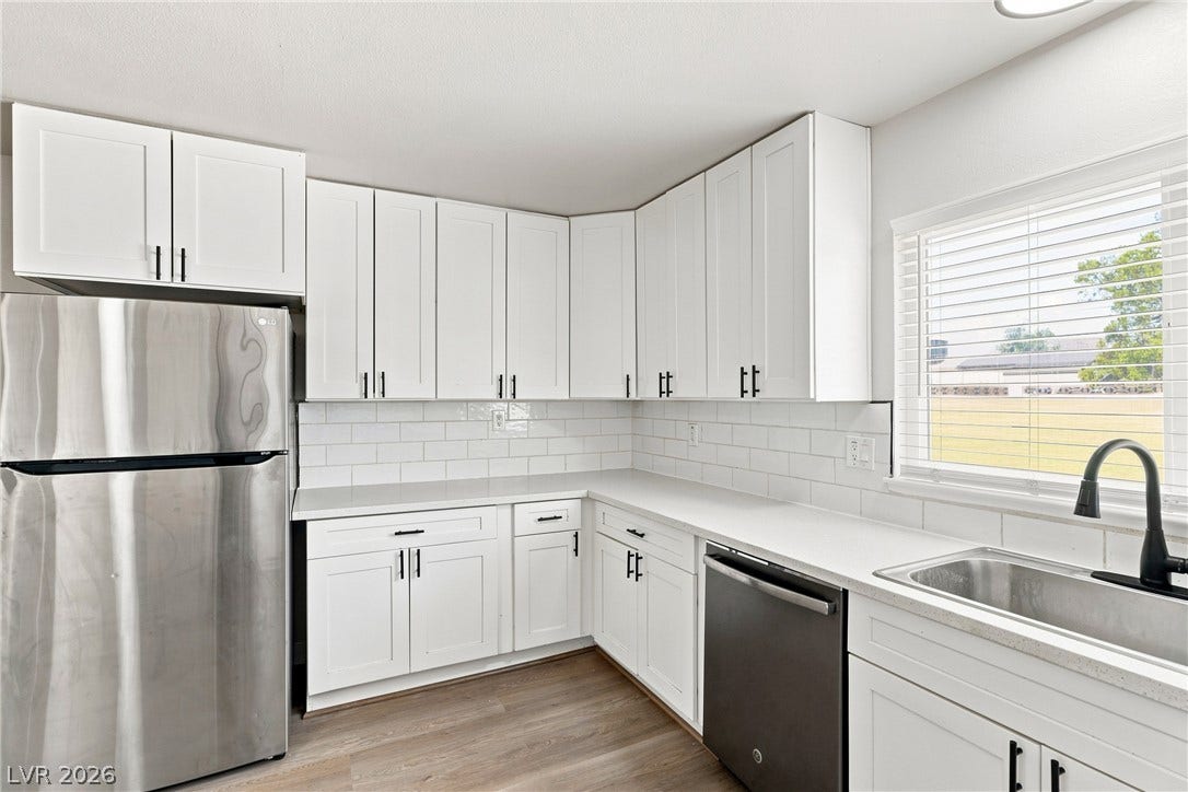 An updated kitchen features white shaker cabinets, solid surface countertops, and stainless steel appliances.