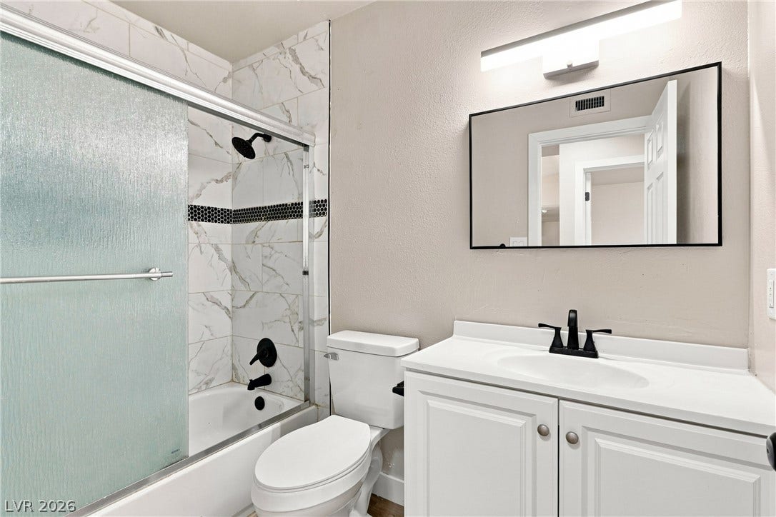 Crisp white cabinetry contrasts with dark plumbing fixtures in this fully tiled bathroom.